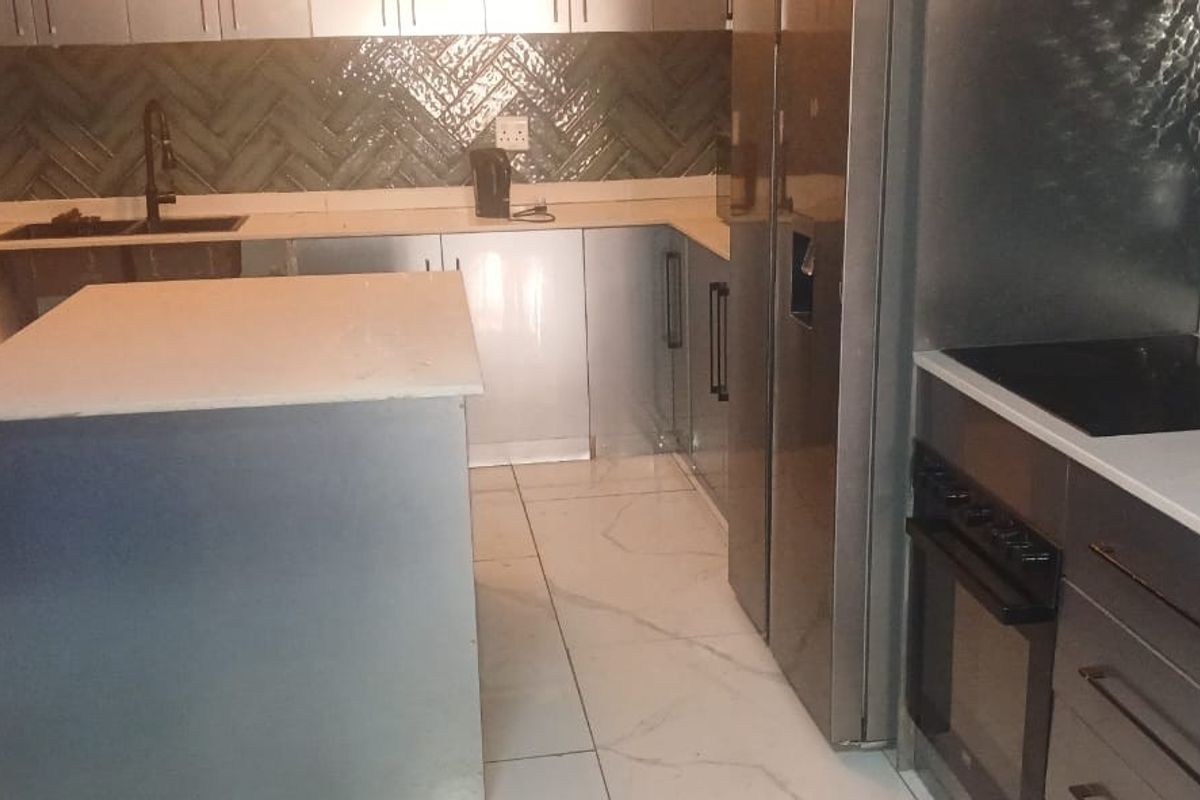 Modern kitchen featuring a central island, stone countertops, herringbone tile backsplash, built-in oven, electric hob, and sleek fitted cabinetry with porcelain floor tiles.