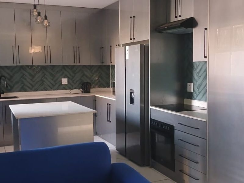Modern kitchen featuring sleek grey cabinetry, a central island, stone countertops, and a stylish herringbone tile backsplash with integrated appliances.