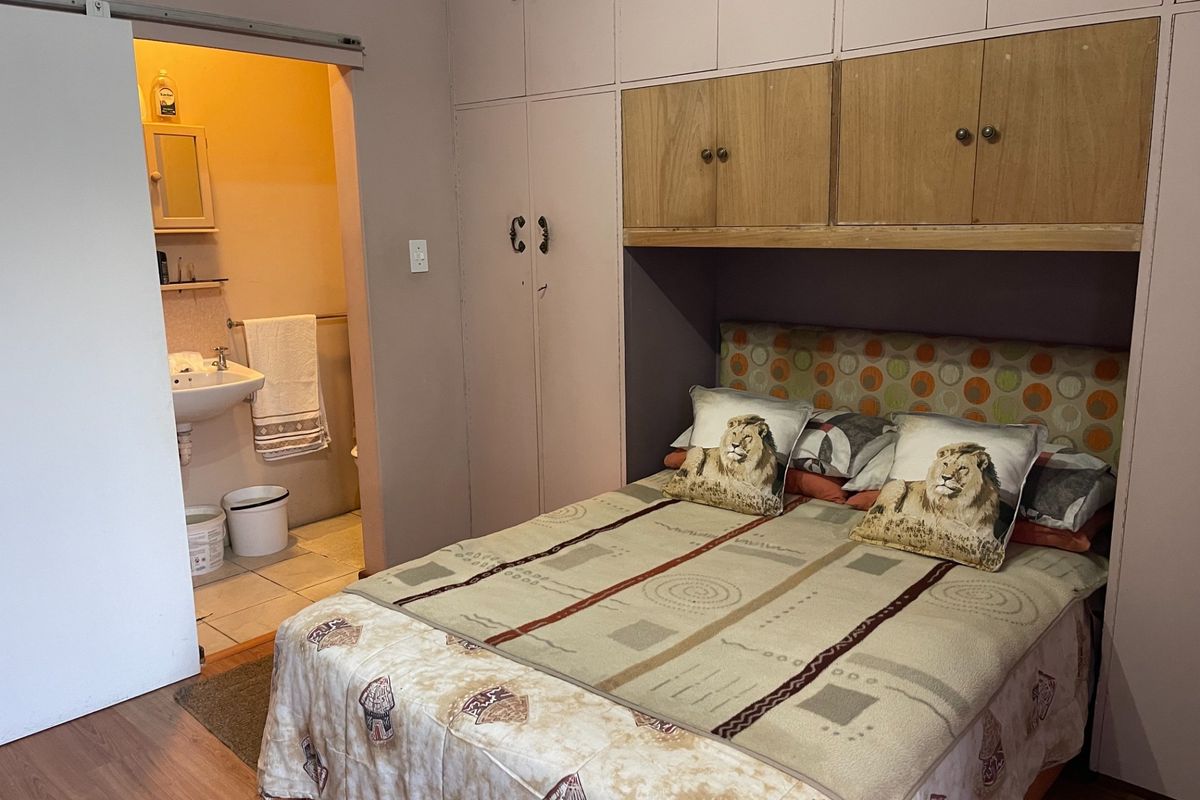 A bedroom featuring built-in cupboards with overhead storage and an adjoining en-suite bathroom with a basin.