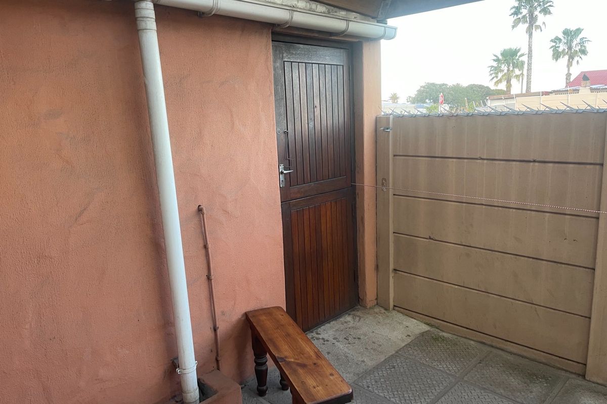 A small rear exterior area featuring a wooden stable door, paved flooring, and a precast concrete boundary wall.