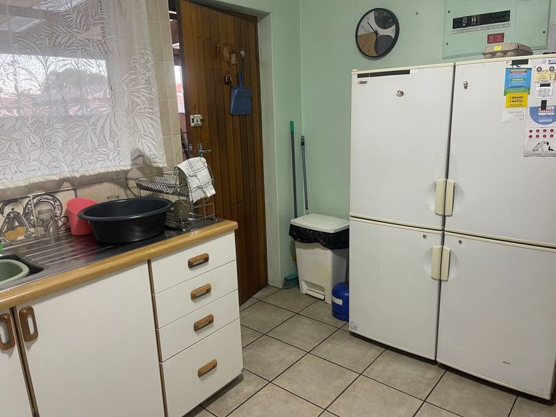 A functional scullery area featuring tiled flooring, built-in cabinetry with a stainless steel sink, and an accessible electrical distribution board.