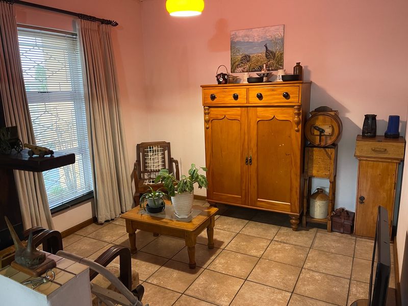 A living room featuring tiled flooring and large windows with blinds, providing a functional space with neutral wall finishes.