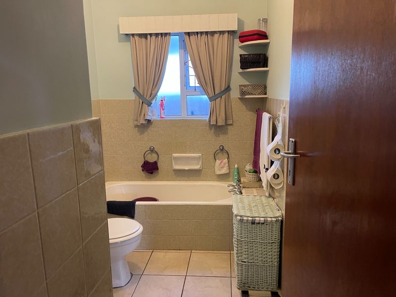 A functional bathroom featuring a built-in bathtub, ceramic tiling, and a standard toilet, offering a practical layout with natural light from the window.