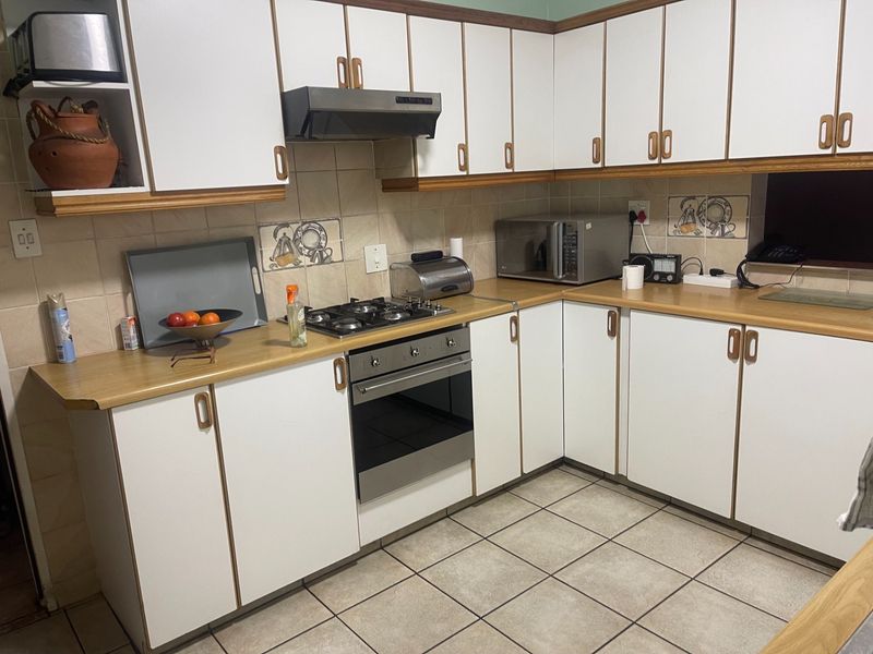 A functional kitchen featuring white cabinetry with wood trim, laminate countertops, a built-in oven, gas hob, and tiled flooring.