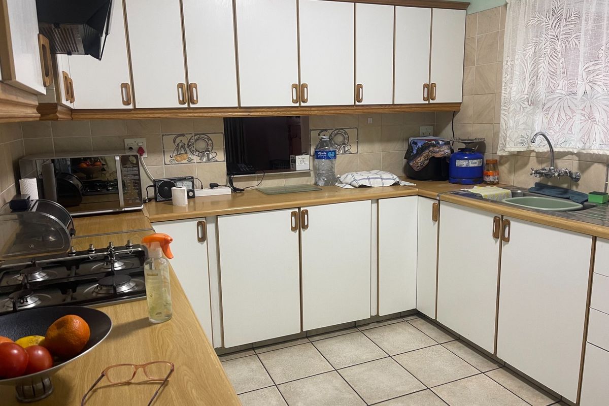 A functional kitchen featuring white cabinetry with wood trim, laminate countertops, a gas hob, and tiled flooring.
