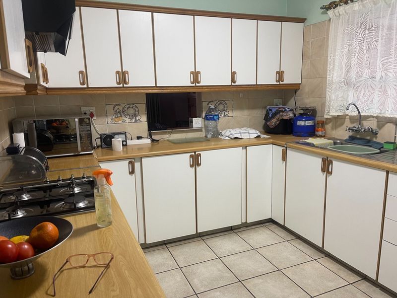 A functional kitchen featuring white cabinetry with wood trim, laminate countertops, a gas hob, and tiled flooring.