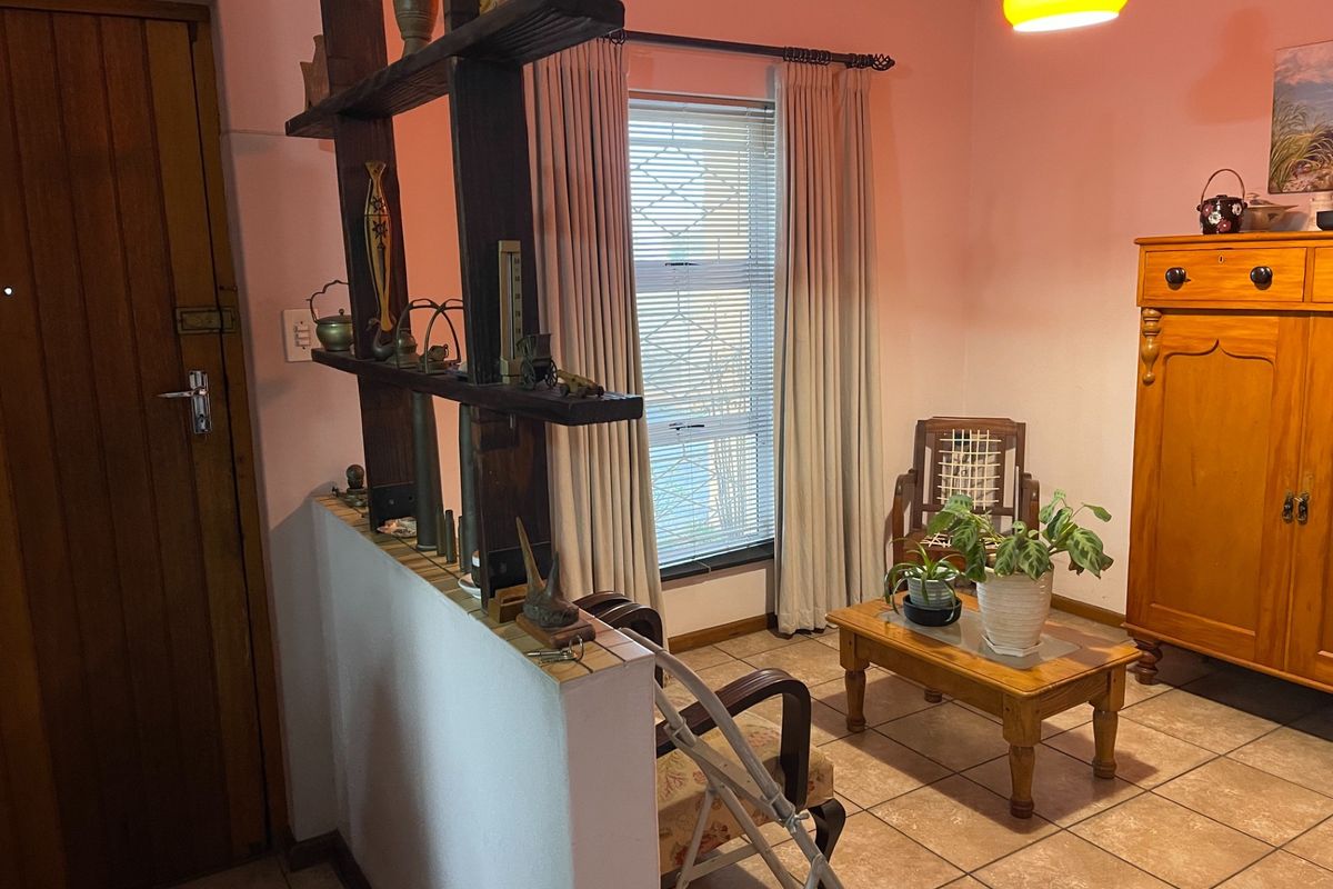 A living area featuring tiled flooring, a timber entrance door, and a built-in wooden room divider, providing a functional and traditional layout.