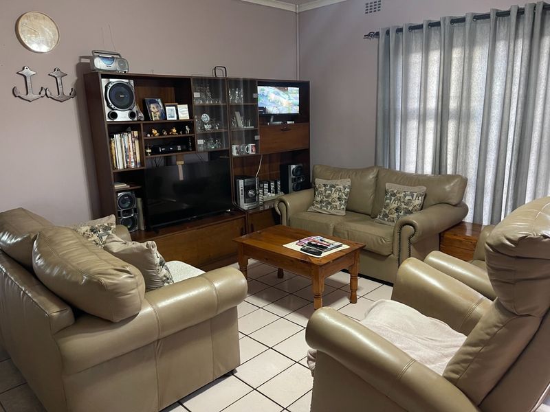 A comfortable living room featuring tiled flooring and large windows with curtains, providing a functional and well-lit space for relaxation.