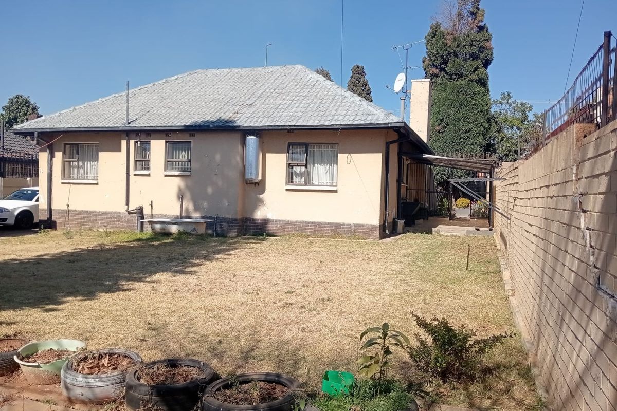 Rear view of the property featuring a tiled roof, solar geyser, and a brick boundary wall with a small covered patio area.
