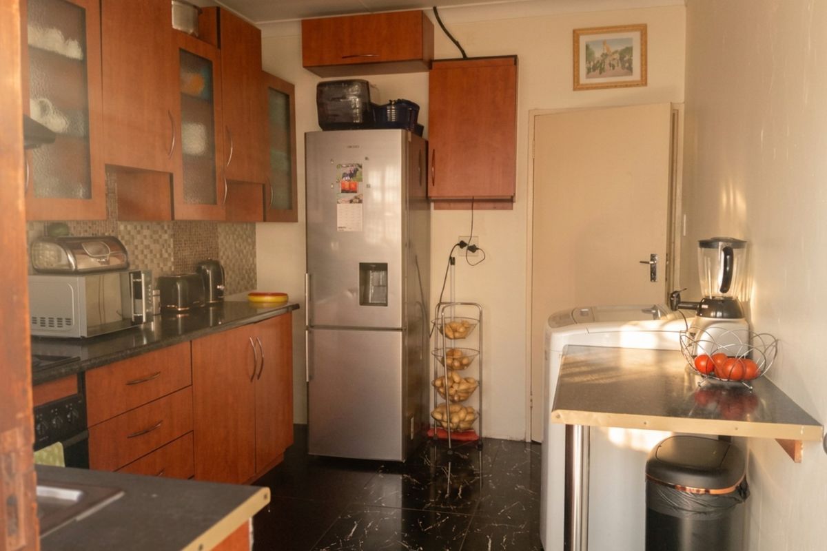 A functional kitchen featuring wooden cabinetry, dark laminate countertops, mosaic tile backsplash, and black floor tiles with integrated cooking appliances.
