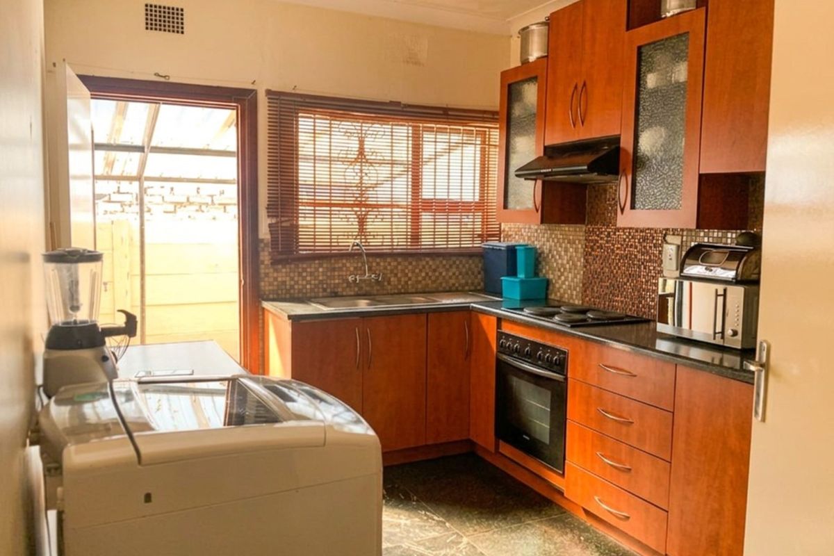 Functional kitchen featuring wood-finish cabinetry, dark countertops, tiled backsplash, and integrated cooking appliances with direct access to an outdoor area.