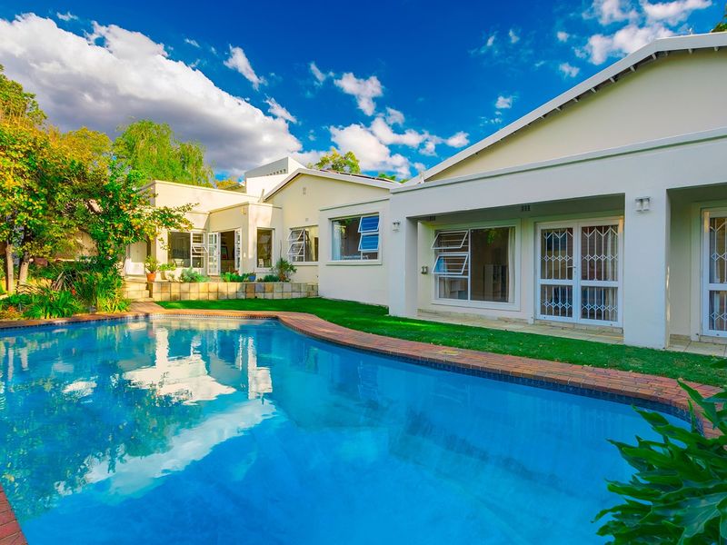 A well-maintained rear exterior view featuring a swimming pool with brick coping, adjacent lawn, and access to the home via sliding doors and security gates.