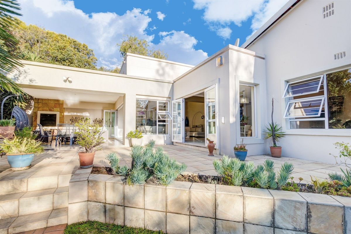 A well-maintained rear patio area featuring a built-in braai, stone cladding, and seamless indoor-outdoor flow through large glass doors.