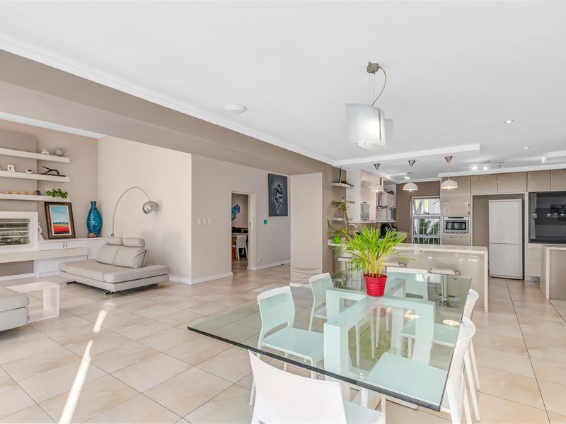 Spacious open-plan living, dining, and kitchen area featuring modern cabinetry, integrated appliances, tiled flooring, and built-in shelving units.