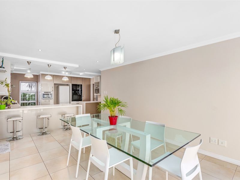 Modern open-plan kitchen and dining area featuring a breakfast bar, sleek cabinetry, built-in appliances, and neutral tiled flooring.