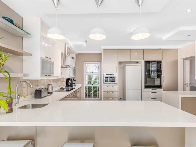 Modern kitchen featuring sleek high-gloss cabinetry, stone countertops, integrated appliances, and stylish pendant lighting, offering a clean and functional culinary space.