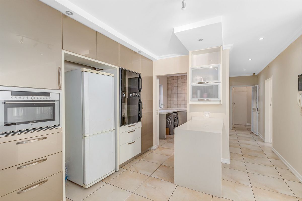 Modern kitchen featuring high-gloss cabinetry, built-in oven and microwave, stone countertops, and tiled flooring, with an adjacent scullery area.