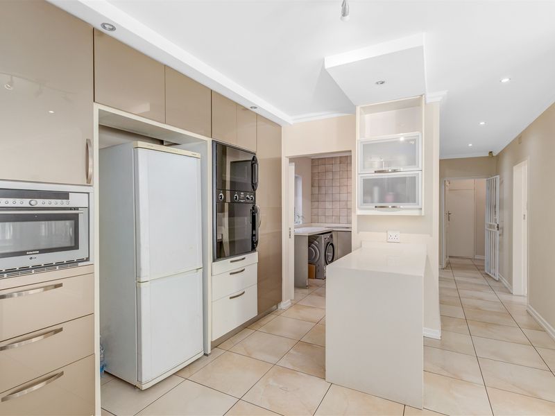 Modern kitchen featuring high-gloss cabinetry, built-in oven and microwave, stone countertops, and tiled flooring, with an adjacent scullery area.