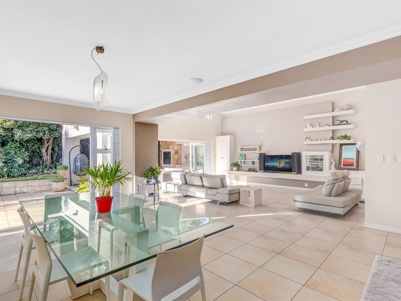 Spacious open-plan living and dining area featuring large format floor tiles, built-in shelving, and seamless access to the outdoor patio through sliding glass doors.