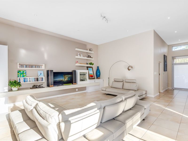 Spacious living room featuring neutral tiled flooring, built-in shelving units, and recessed lighting, creating a bright and open atmosphere.