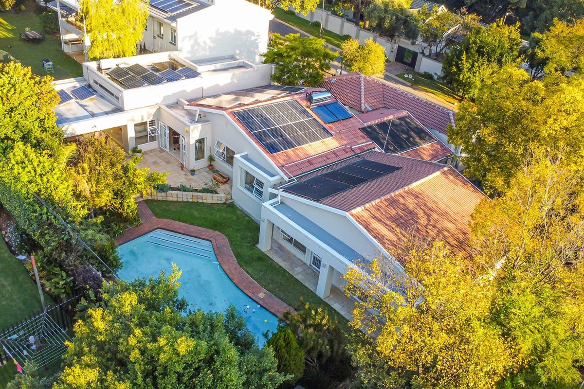 Aerial view of a residential property featuring a tiled roof with extensive solar panel installations, a swimming pool, and a landscaped garden.