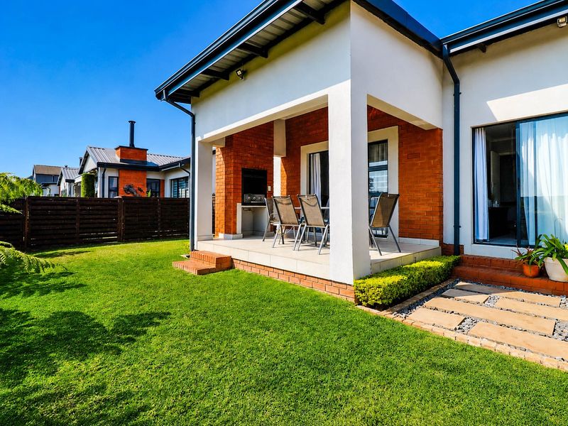 A covered patio featuring a built-in braai, overlooking a well-maintained garden with paved pathways and modern brick and plaster exterior finishes.