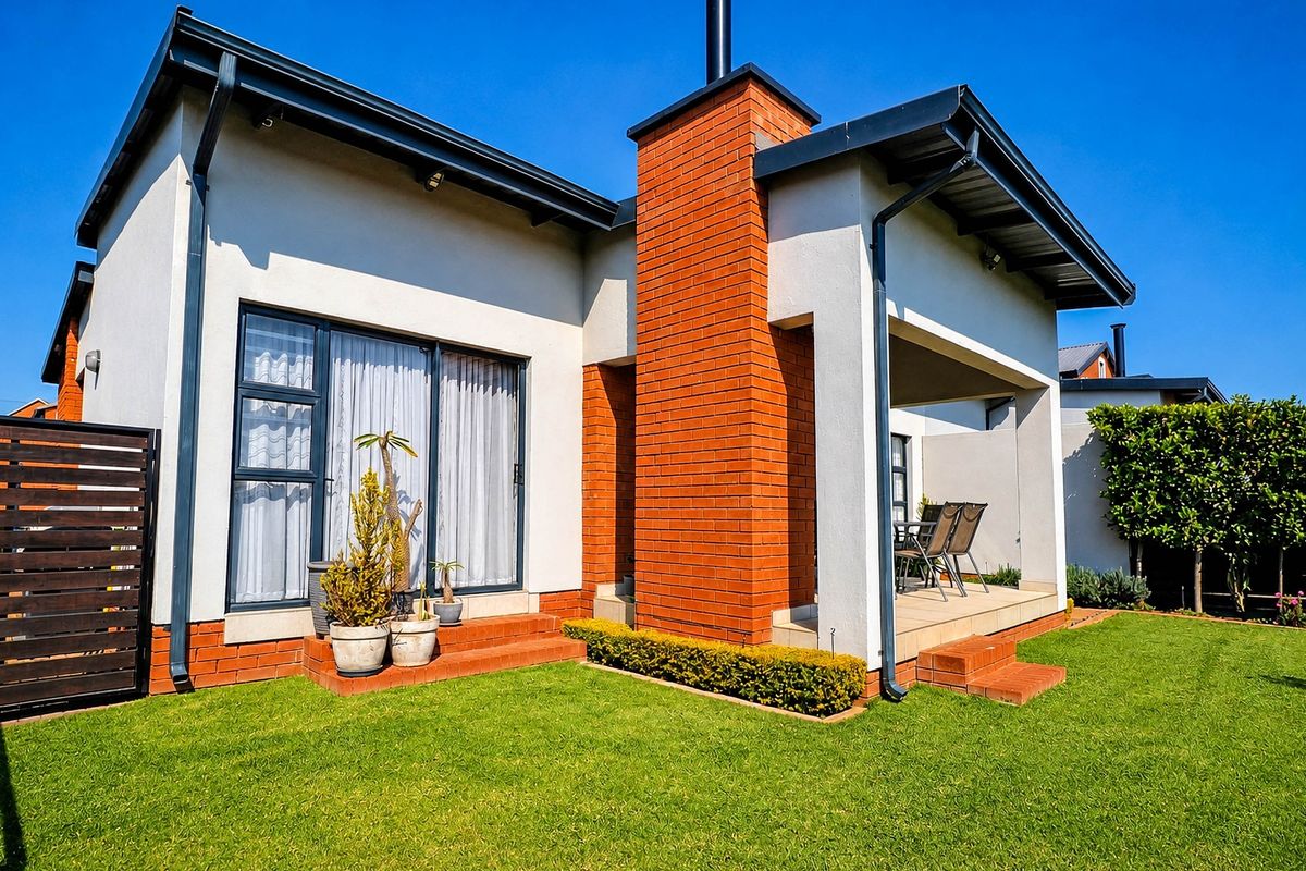 Rear view of the townhouse featuring a covered patio, brick chimney, and well-maintained lawn area.
