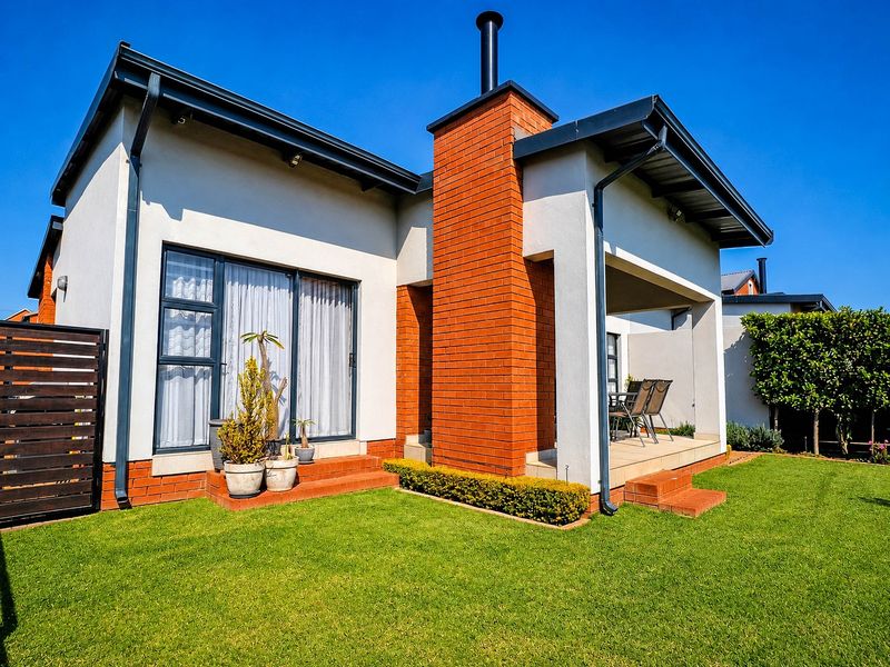 Rear view of the townhouse featuring a covered patio, brick chimney, and well-maintained lawn area.