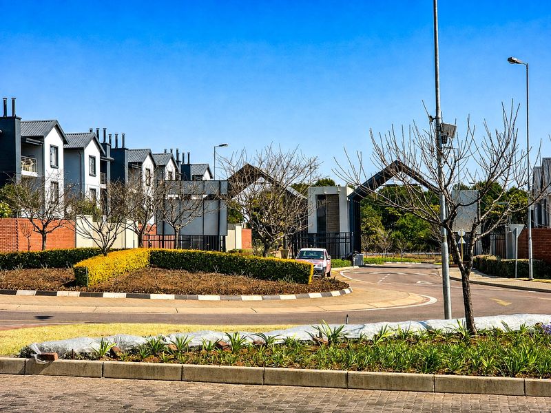 A view of the gated entrance and roundabout leading into the townhouse complex, featuring landscaped verges and modern architectural design.