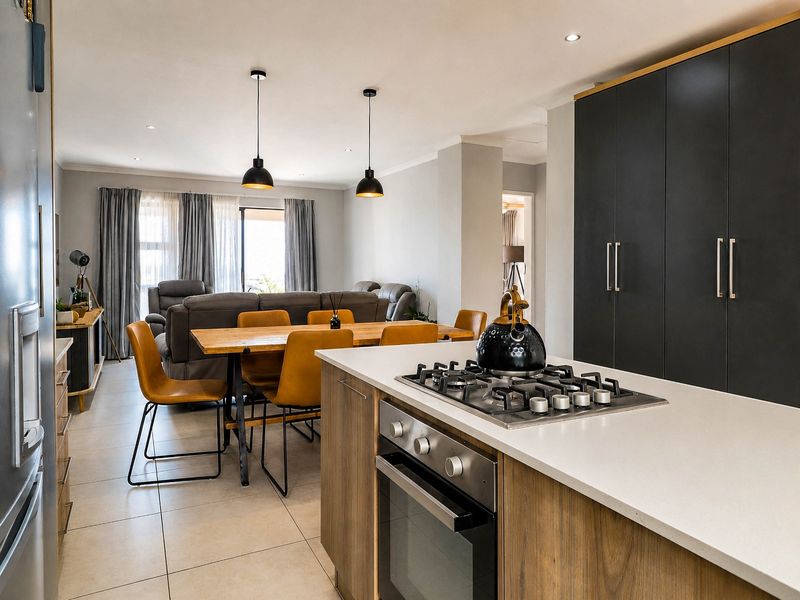 Modern open-plan living area featuring a contemporary kitchen with stone countertops, gas hob, built-in oven, and seamless flow into the dining and lounge space.