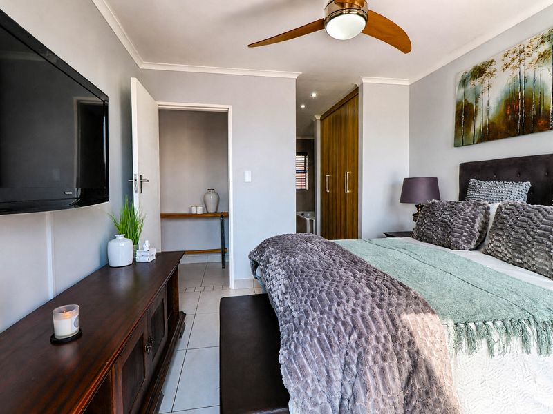 A well-maintained bedroom featuring tiled flooring, a ceiling fan, and built-in cupboards, with an adjoining space visible through the doorway.