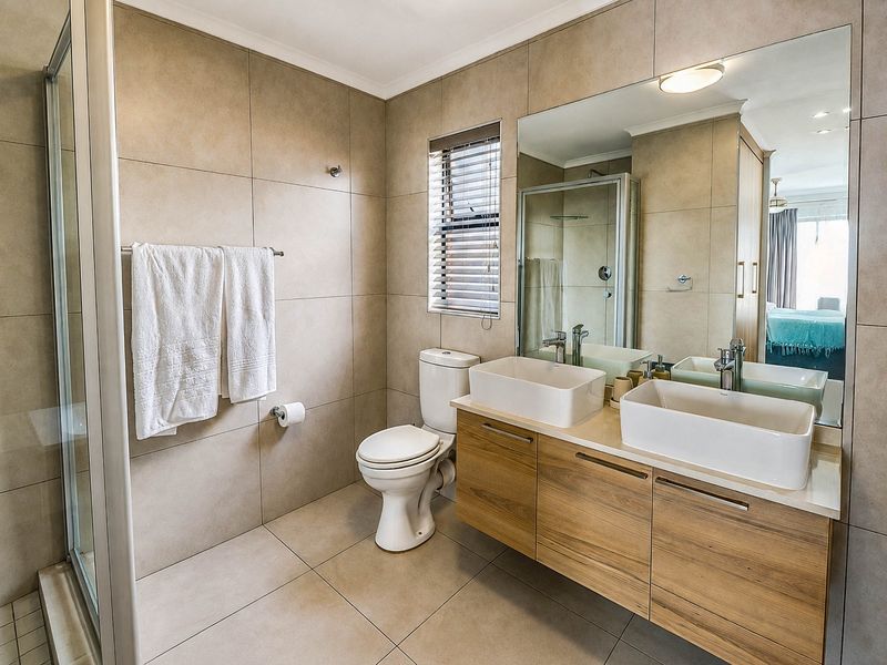 Modern bathroom featuring a double vanity with vessel sinks, a glass-enclosed shower, large wall mirror, and neutral floor-to-ceiling tiling.
