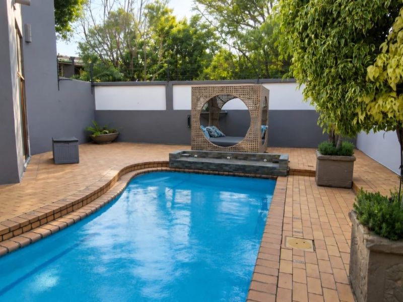 A well-maintained outdoor pool area featuring brick paving, a raised pool edge, and a secure boundary wall in a private garden setting.