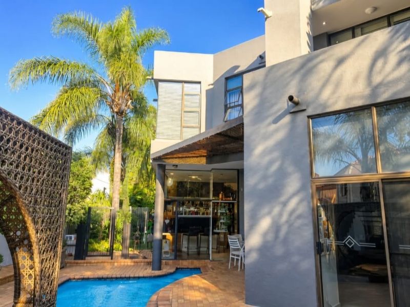 Rear exterior view featuring a swimming pool, brick paved patio area, and modern grey facade with large sliding glass doors.