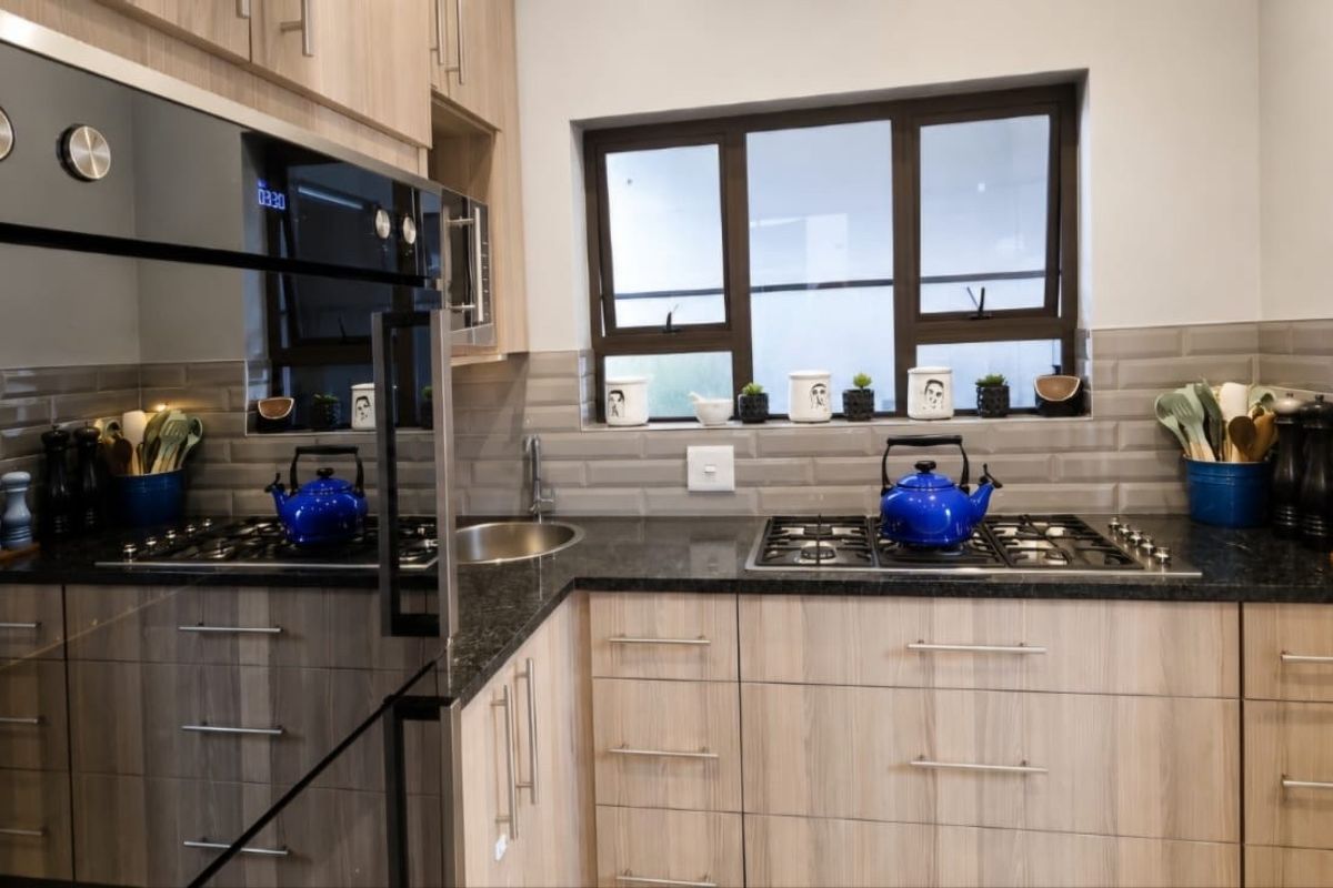 Modern kitchen featuring wood-finish cabinetry, granite countertops, subway tile backsplash, and integrated stainless steel appliances.