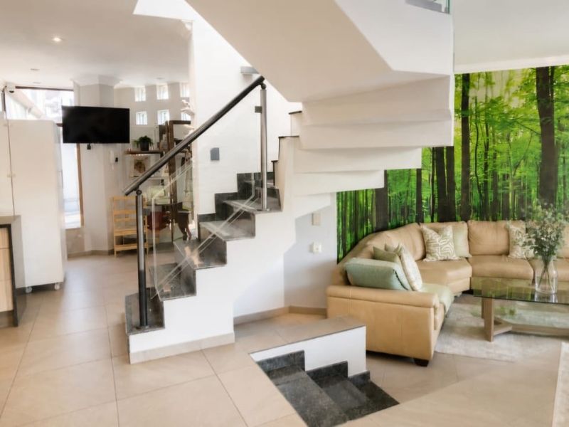 Open-plan living area featuring a modern staircase with glass balustrade, tiled flooring, and a contemporary kitchen with wood-finish cabinetry.