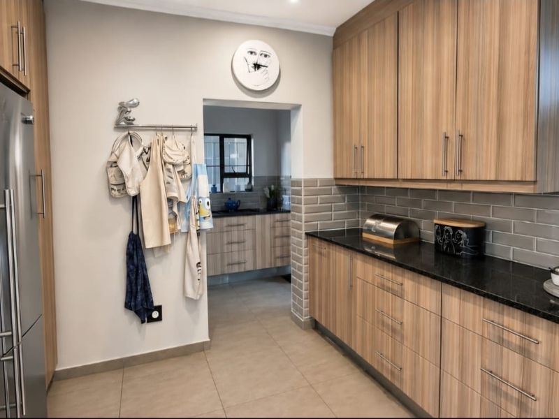 Modern kitchen featuring wood-grain cabinetry, granite countertops, and a subway tile backsplash, with an adjoining scullery area.