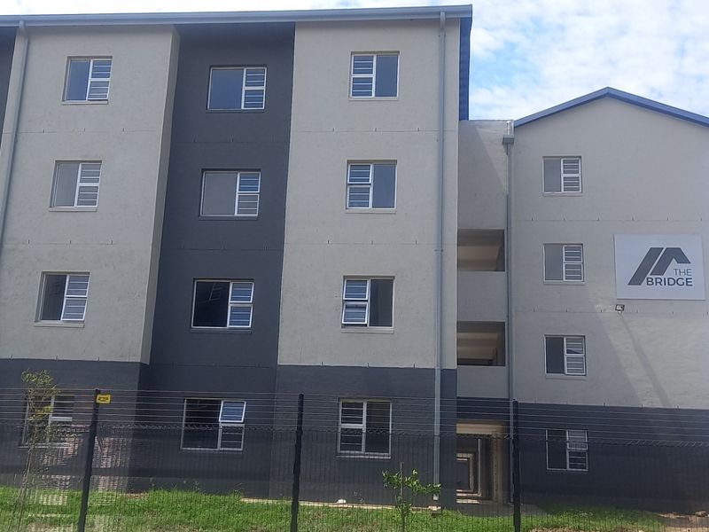 Exterior view of The Bridge apartment complex featuring modern multi-story architecture with secure perimeter fencing and aluminium window frames.