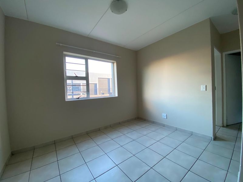 A clean, empty bedroom featuring neutral tiled flooring, a large aluminium-framed window, and a simple ceiling light fixture.