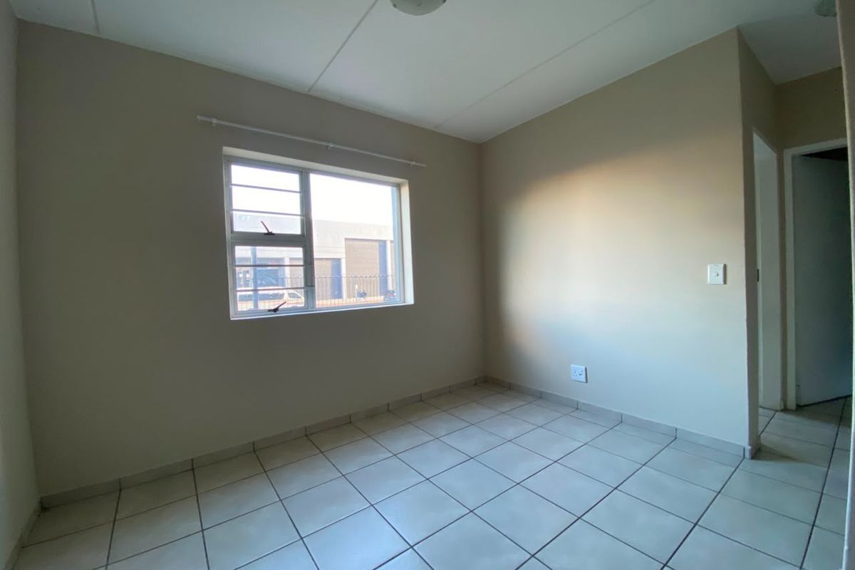 A clean, empty bedroom featuring neutral tiled flooring, a large aluminium-framed window, and a simple ceiling light fixture.