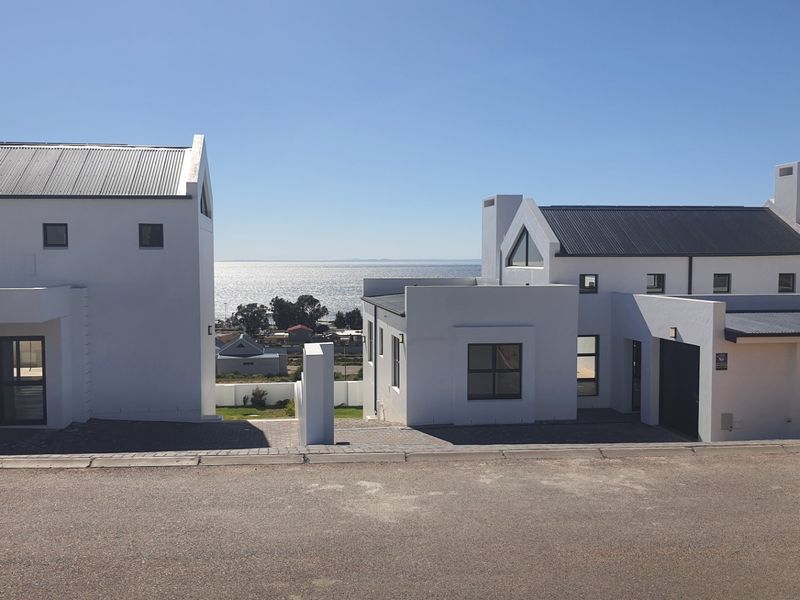 Front elevation of modern residential properties featuring white rendered facades, corrugated metal roofing, and paved driveway access with coastal views.