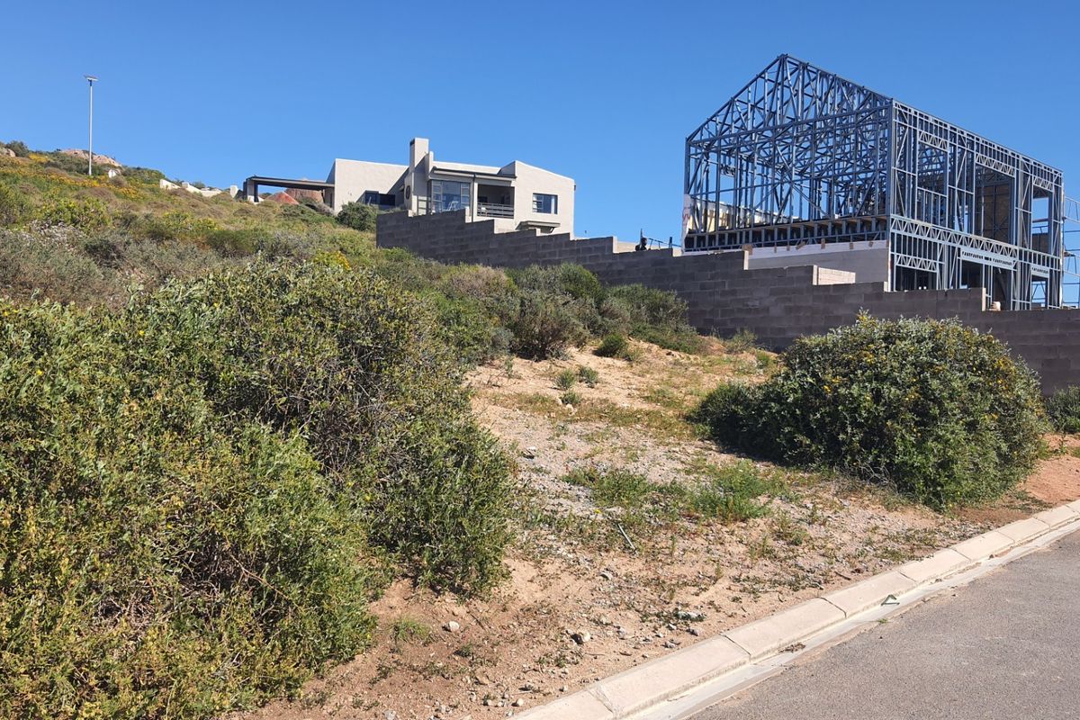 A vacant residential plot featuring a partially constructed steel frame building and a concrete retaining wall on a sloped landscape.