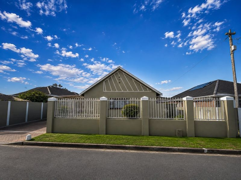 Front elevation of a well-maintained house featuring a secure perimeter wall with metal fencing and a paved driveway.