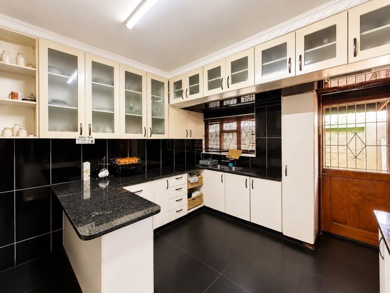 A well-maintained kitchen featuring contrasting black and white cabinetry, granite countertops, a double sink, and ample storage space with glass-fronted upper cabinets.