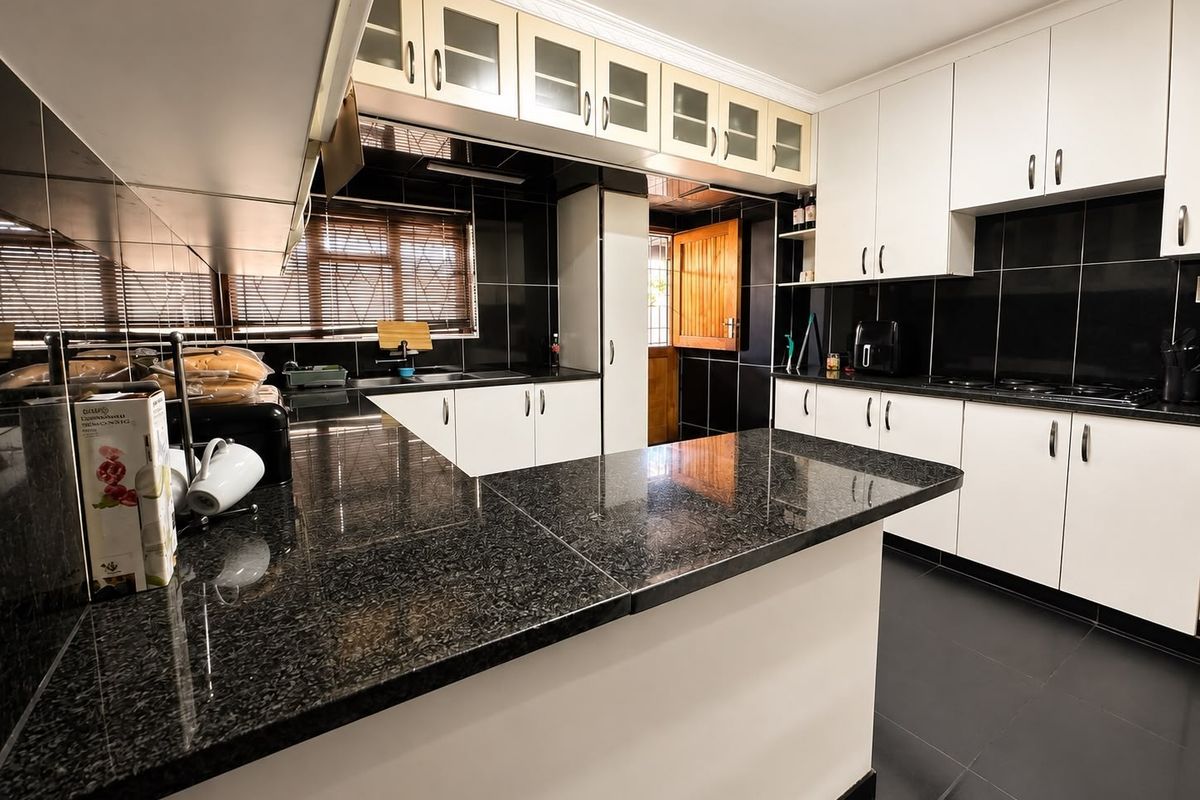 Modern kitchen featuring contrasting white cabinetry, black granite countertops, and a tiled backsplash with ample storage and workspace.