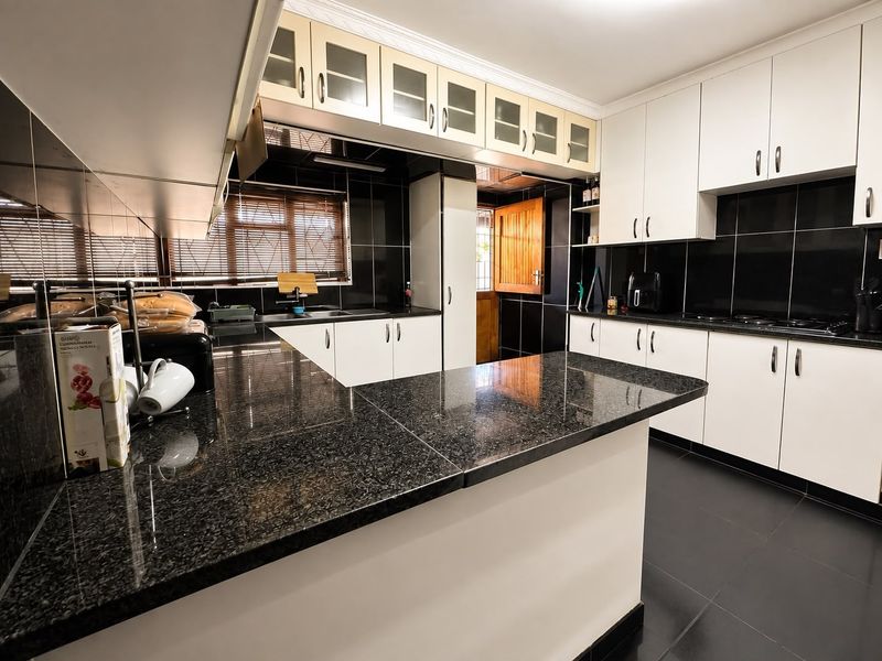 Modern kitchen featuring contrasting white cabinetry, black granite countertops, and a tiled backsplash with ample storage and workspace.