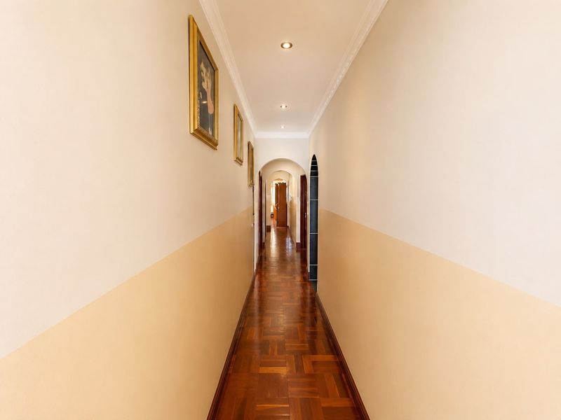 A well-maintained hallway featuring classic parquet flooring, recessed ceiling lighting, and decorative coving, leading through an arched transition to further living areas.