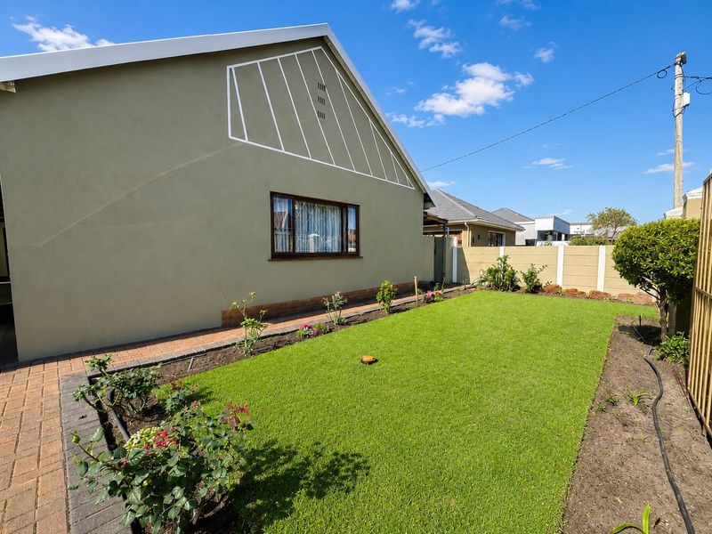 A well-maintained rear garden featuring a neat lawn, paved walkway, and secure precast concrete boundary wall.