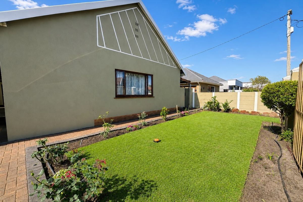 A well-maintained rear garden featuring a neat lawn, paved walkway, and secure precast concrete boundary wall.