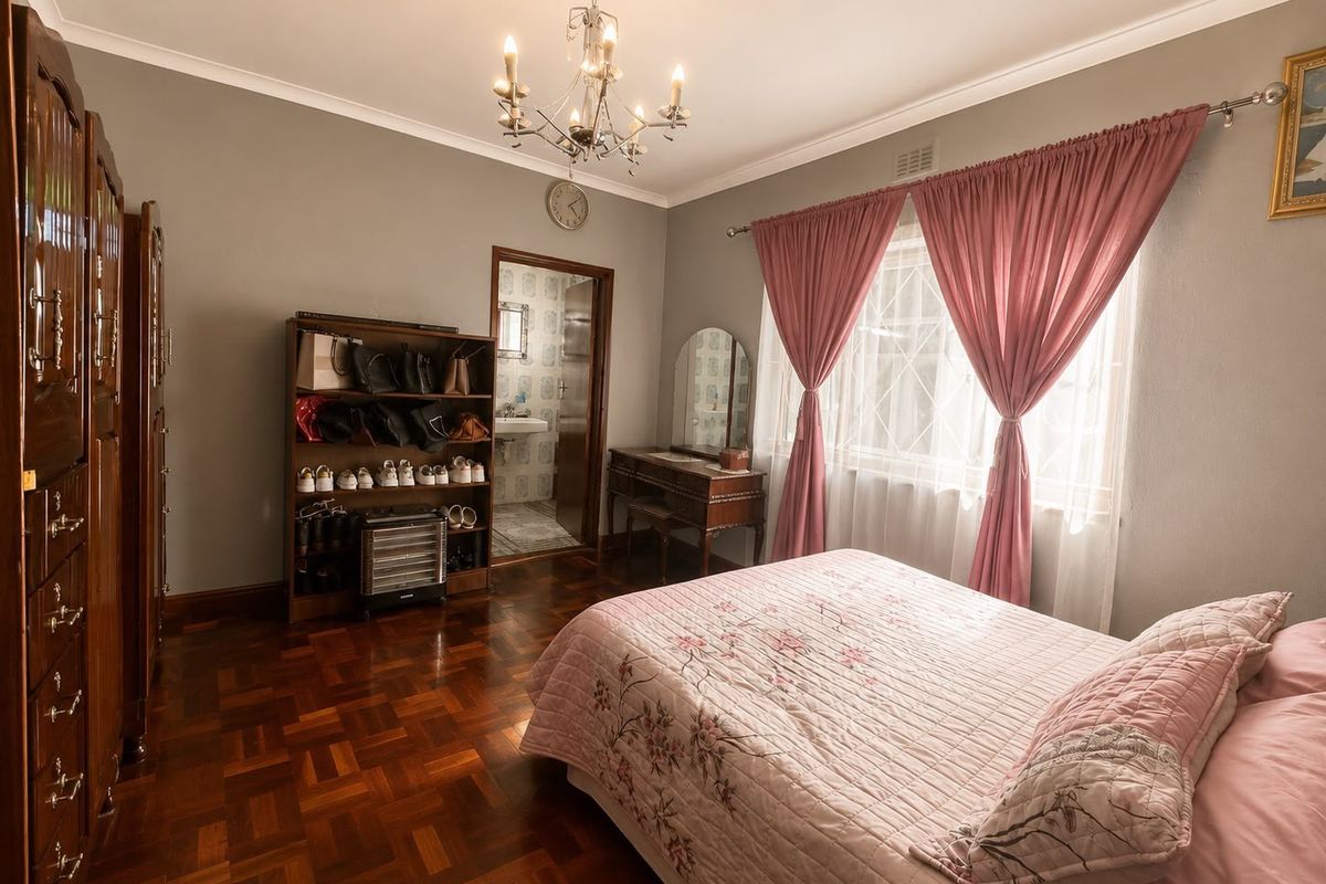Spacious bedroom featuring classic parquet flooring, elegant ceiling chandelier, and direct access to an en-suite bathroom.
